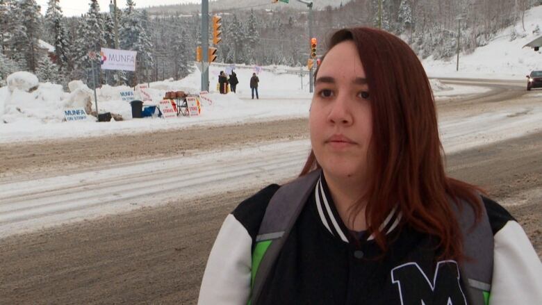 A woman wearing a black and white jacket standing on a snowy road. 