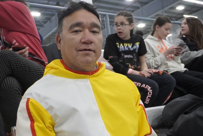 A man in a white and yellow sweater sits amongst a crow. 