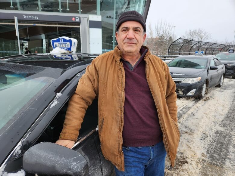 Man in hat stands in front of cab. 