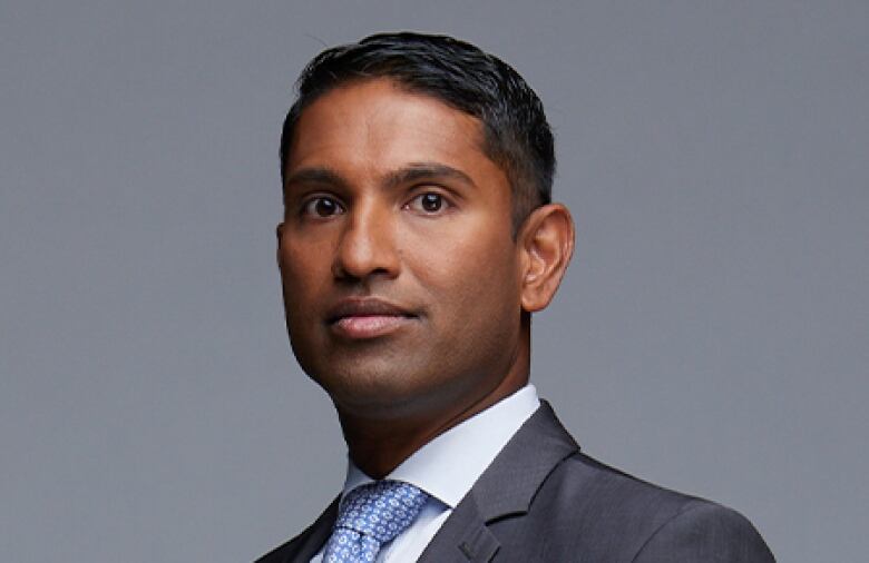 Steven D'Souza is pictured in a posed headshot wearing a blue tie and grey suit.