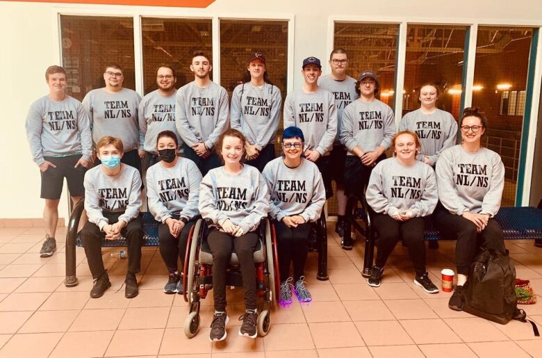 A basketball team poses for a team photo. Players and coaches are all wearing grey crewneck sweaters that read 'Team NL/NS