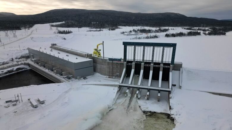 Water pours through the spillgates of the Muskrat Falls dam, whose reservoir is iced over and covered with snow.