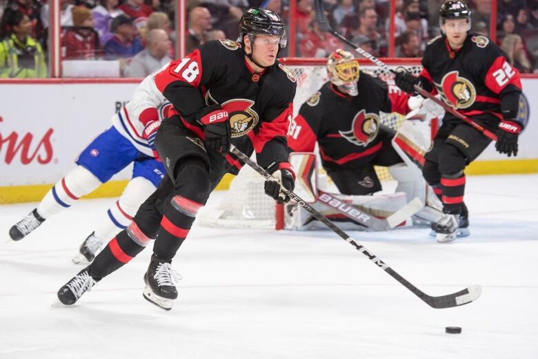 A hockey player hustles to skate the puck out of his end of the ice.