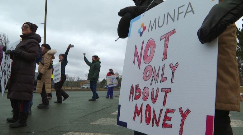 Strikers walk along a street. One holds a sign which reads not only about money. 