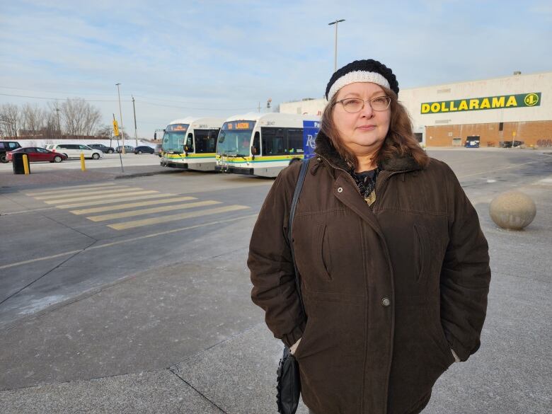 A woman wearing a brown jacket standing in front of public transit buses