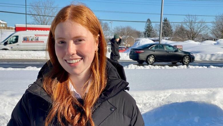 A young woman stands in front of a snowy road. 