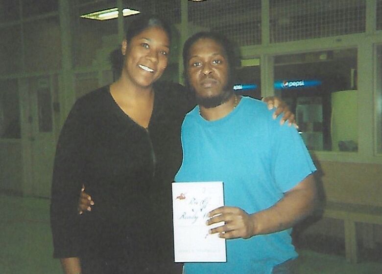 A woman and a man holding a book hug for a photo. 