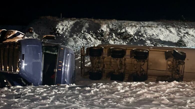 A truck overturned on its side in the snow in the dark.