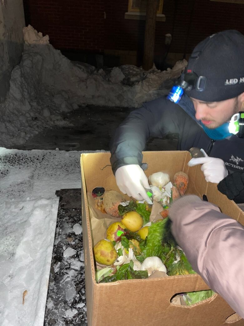 Jasmin Cartier digs through a box of produce taken from a local grocery store dumpster.