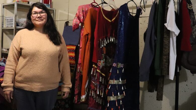 A woman stands next to her collection of jingle dresses, which show off a variety of colours.