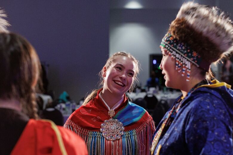 People dressed in traditional clothing smile as they talk to each other.