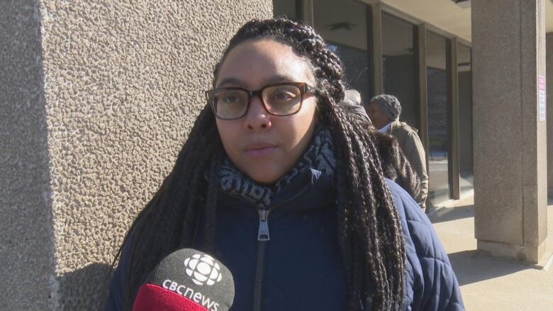 A woman with glasses stands in front of a building.