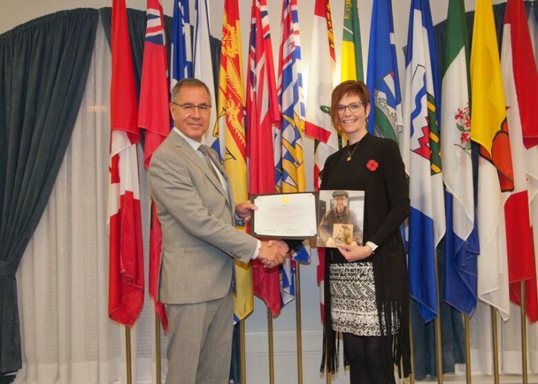 Valerie Guillemin holds a photo of her father Adrian K. Paton as she accepts his posthumous Saskatchewan Heritage Award for his book 'An Honest, Genial and Kindly People' from Saskatchewan Lieutenant Governor Russell Mirasty.