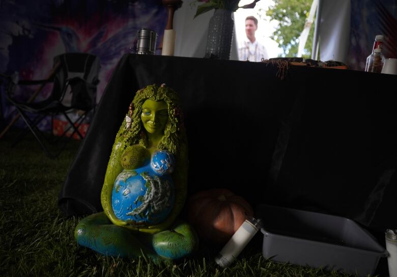 A green statue of a goddess depicting mother earth sits on the grass in a chapel of the Hummingbird psychedelic church.