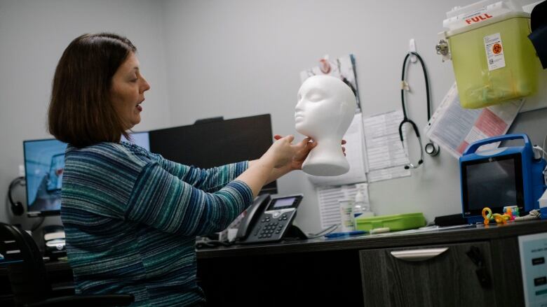 A woman in a blue shirt holds up a styrofoam head to demonstrate strangulation injuries. 