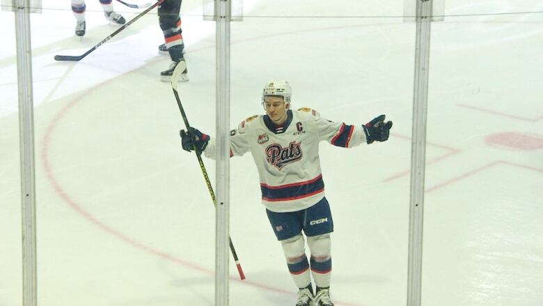 A hockey player is skating on the ice toward the boards, with his arms spread out and stick in hand, as he celebrates scoring a goal. 