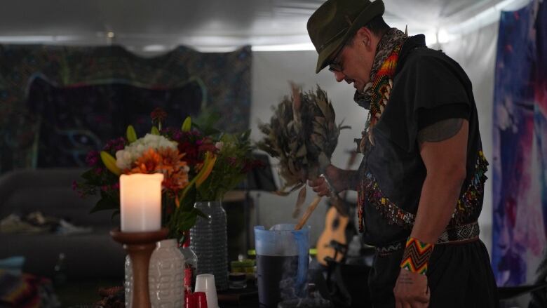 A shaman holds a bundle of ayahuasca at an altar with burning candle.