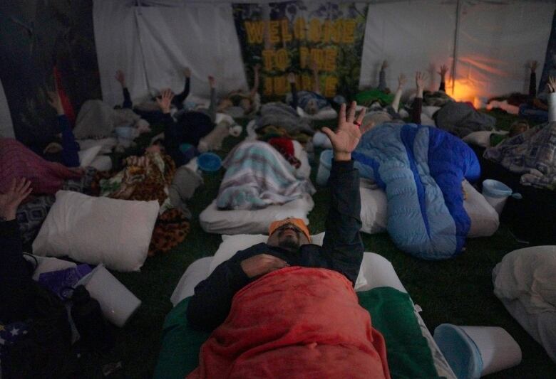 A man points his hand up in the sky as he lays on a matt during an ayahuasca church ceremony.