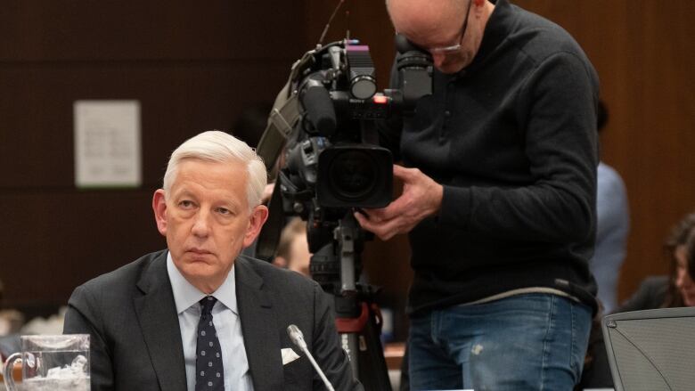 A cameraman records Dominic Barton as he waits to appear as a witness at the standing committee on government operations and estimates on Feb. 1, 2023, in Ottawa.