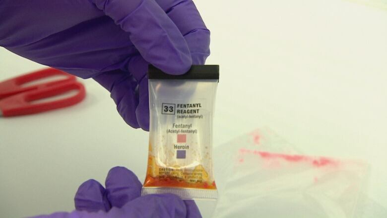 A small package with labels showing fentanyl in red and heroin in blue. The substance inside of the package has turned red.