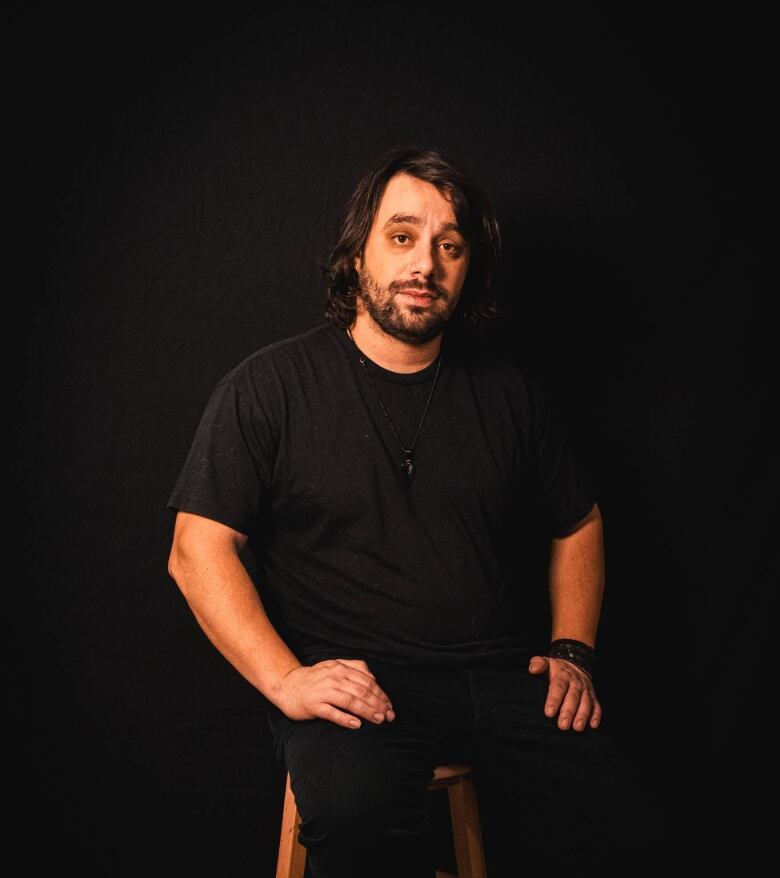 Portrait of man on stool with black background.