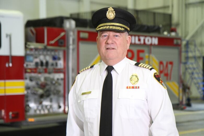 A fire chief stands in front of a fire truck. 