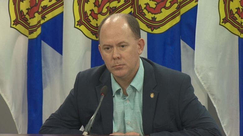 A man in a suit sits at a table with a Nova Scotia flag in the background