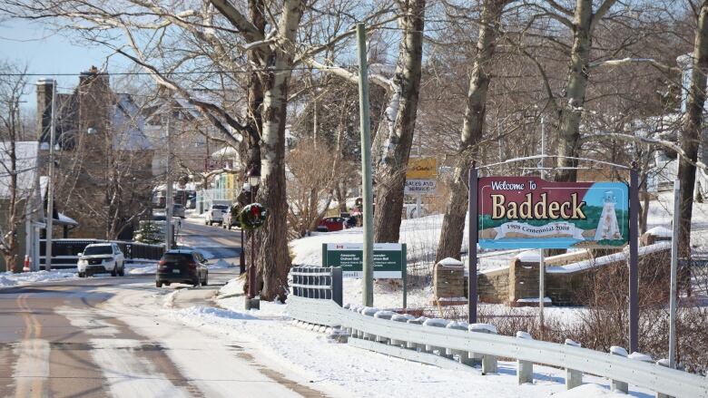 A snowy roadway with two cars driving in opposite directions. There is a sign on the right side of the street that says, 