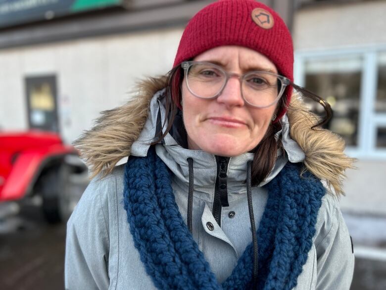 Woman wearing glasses and woollen hat stands outside.