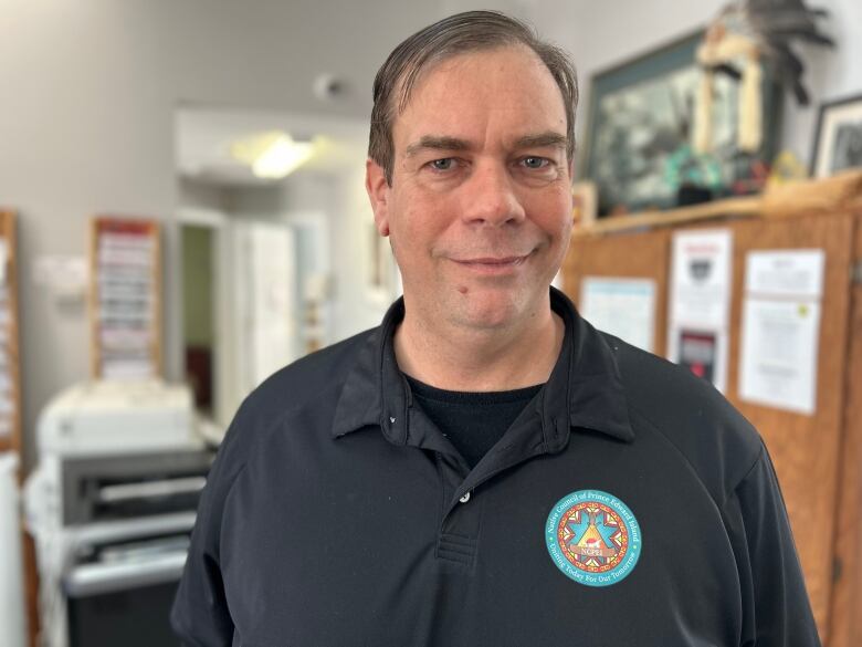 Man with brown hair wearing dark blue shirt stands in office.