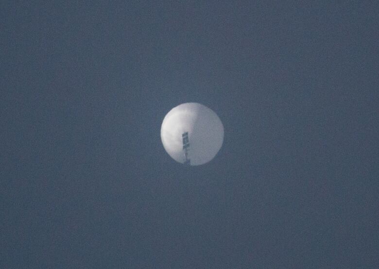 A spherical white balloon flies high in a blue sky. 