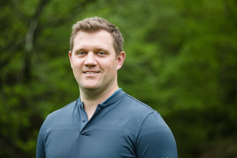 A man in a blue shirt in front of a blurry green background