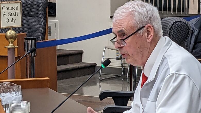 Thunder Bay resident Ray Smith sits at a desk in front of a desk-top microphone in the council chambers at Thunder Bay City Hall while speaking to council about his budget concerns. 