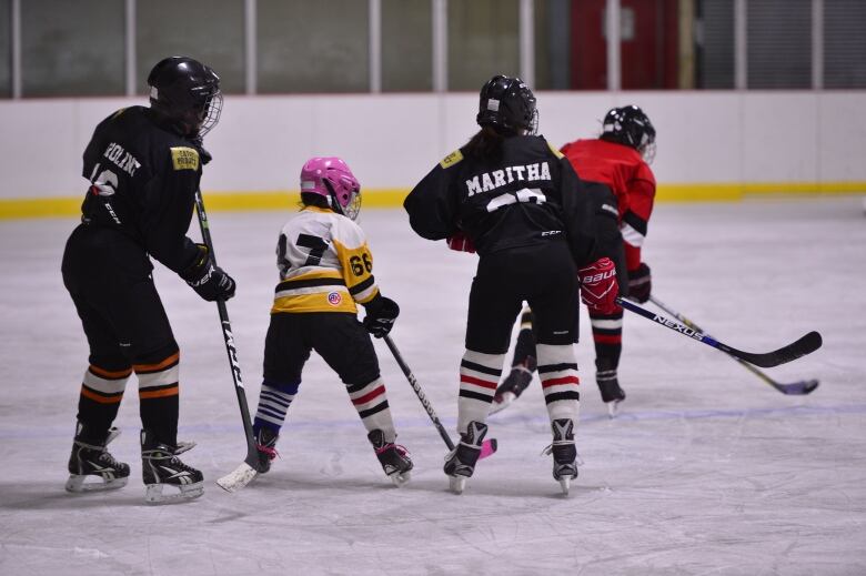 Small hockey player amid three larger ones.