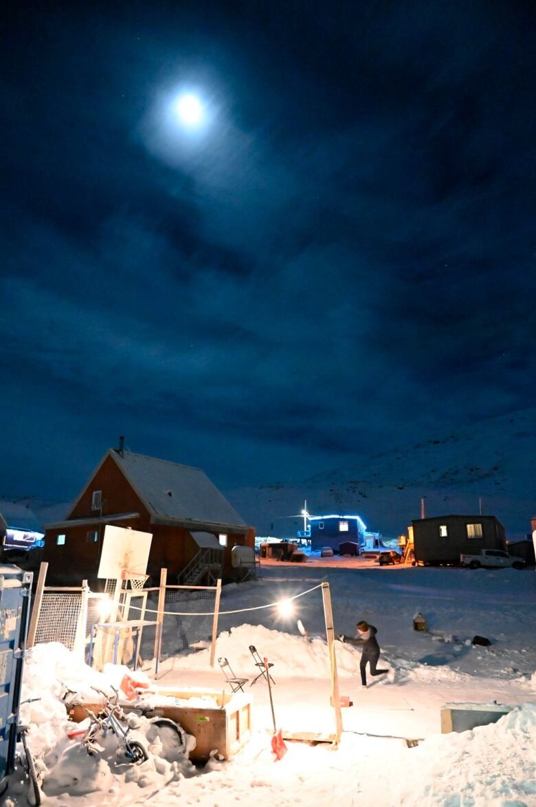 Girl on backyard ice under full moon.