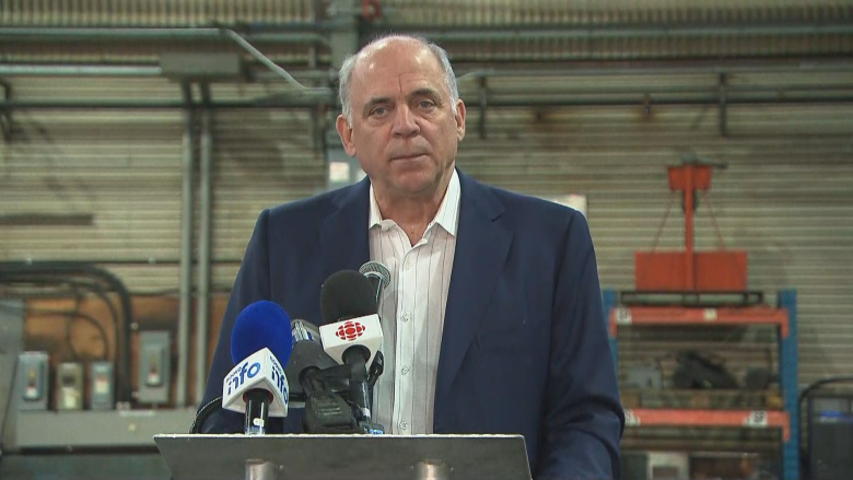 Man in suit in front of microphones, industrial background.