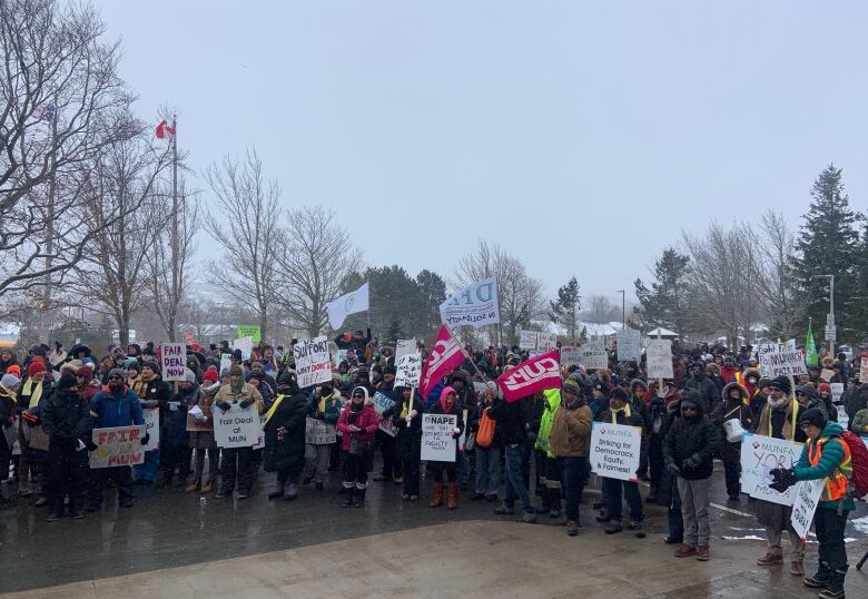 A crowd of people standing in a parking lot, many holding signs in support of MUNFA.