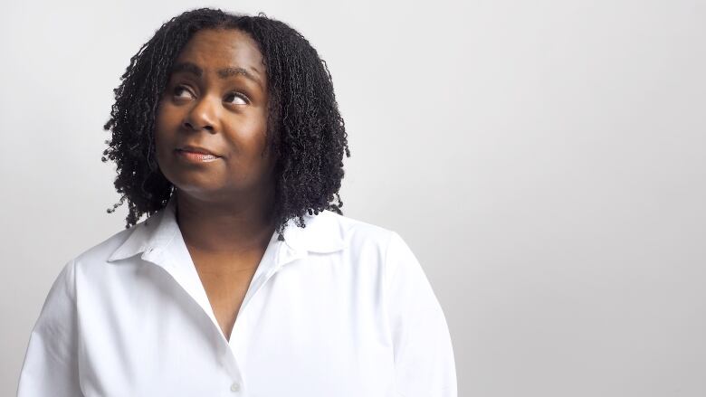 A middle-aged Black woman in a white blouse looks skyward.