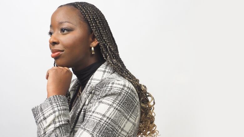 A woman with long braids and wearing a black-and-white plaid jacket stares off in the distance.