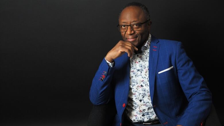 An older Black man in a blue suit looks at the camera.