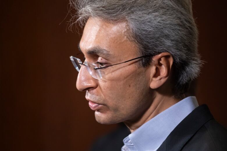 A South Asian man wearing glasses and a suit is pictured in profile.