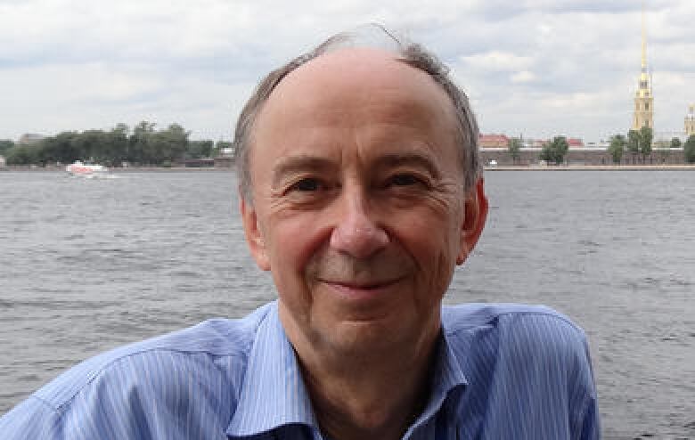 John Gill faces the camera, outside along a shoreline.