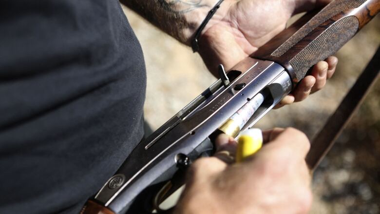 A man's hand inserts a bullet into a hunting rifle.