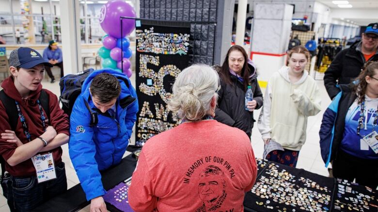 A woman stands facing a crowd, holding numerous commemorative pins in front of her.