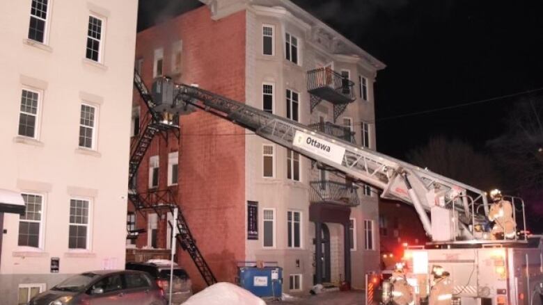 A ladder is extended from a fire truck with firefighters standing beside the truck.