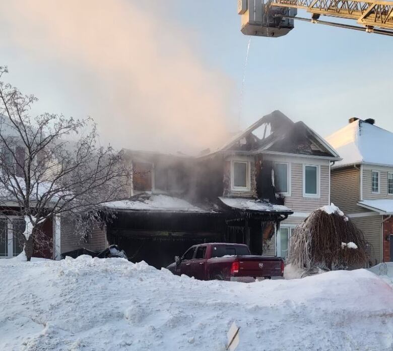 A crane extends to a home with smoke coming from the garage on a snowy street.