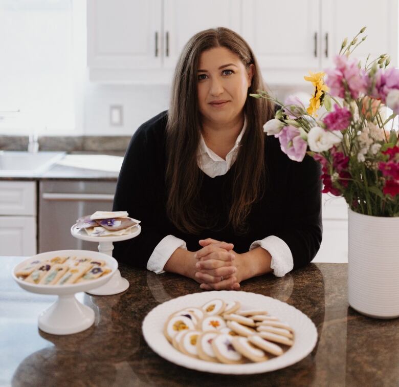 A woman in a black sweater is seated at a table with dishes of pastries in front of her.