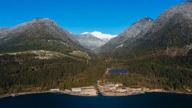 Snowcap mountain appears in the background of a photograph showing an aerial view of an industrial site along a waterfront.