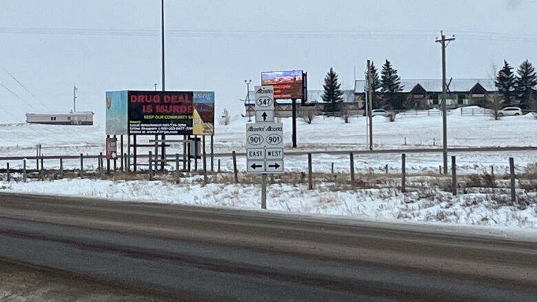 A highway in Alberta with road signs and buildings in the distance.