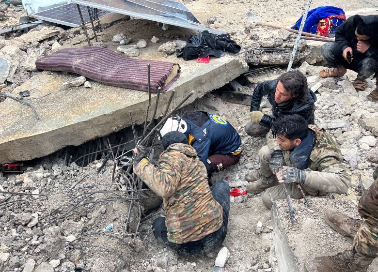 Four men dig through the rubble of a collapsed building, searching for survivors, following an earthquake. 